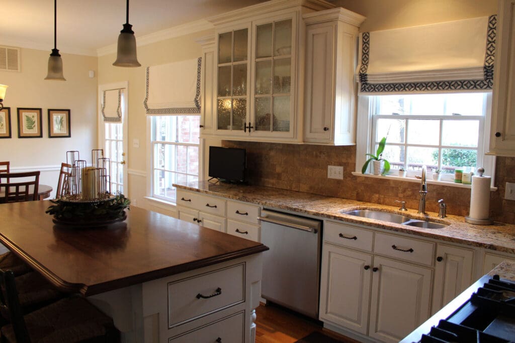 Bright kitchen with white cabinets, granite countertops, a kitchen island, stainless steel appliances, and large windows letting in natural light.