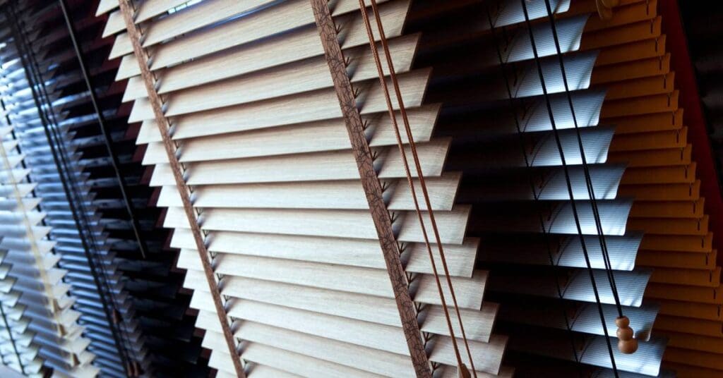 Close-up view of partially open horizontal window blinds, with light filtering through the slats and pull cords hanging on the right.