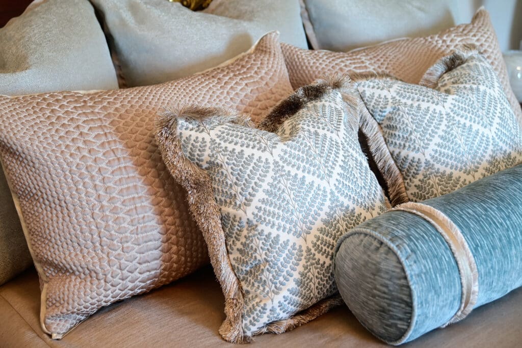 A group of decorative pillows in beige and blue tones, including patterned and textured designs, arranged on a couch or bed.