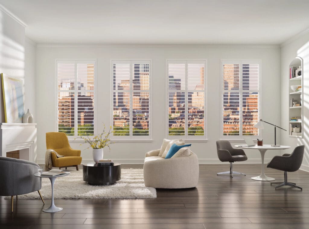 Modern living room with large windows, city skyline view, contemporary furniture in neutral tones, and wood flooring.