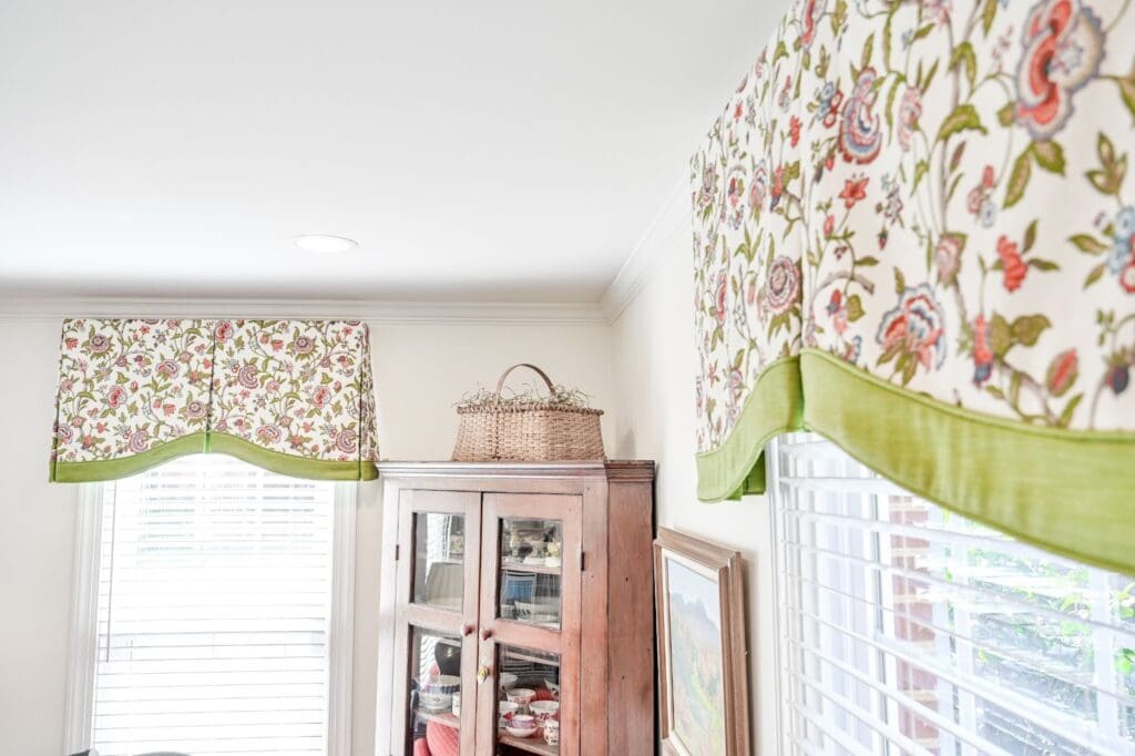 Close-up of custom-made fabric valances with a floral pattern and green border installed over white horizontal blinds.