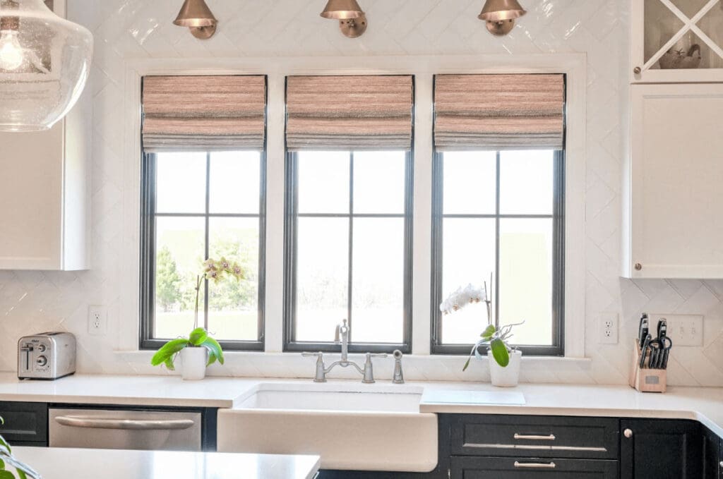 Modern kitchen with three windows over a farmhouse sink, featuring natural woven wood shades for light filtering and privacy.