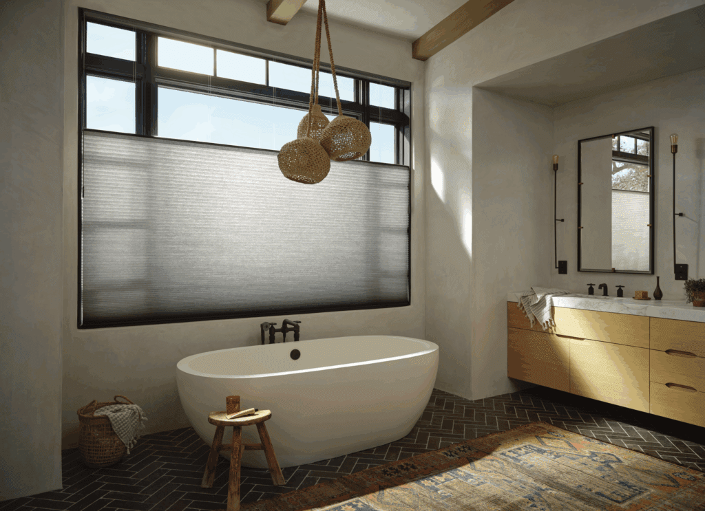 Modern bathroom with freestanding white tub, woven pendant lights, shaded window, wood vanity with double sinks, and herringbone tile floor.