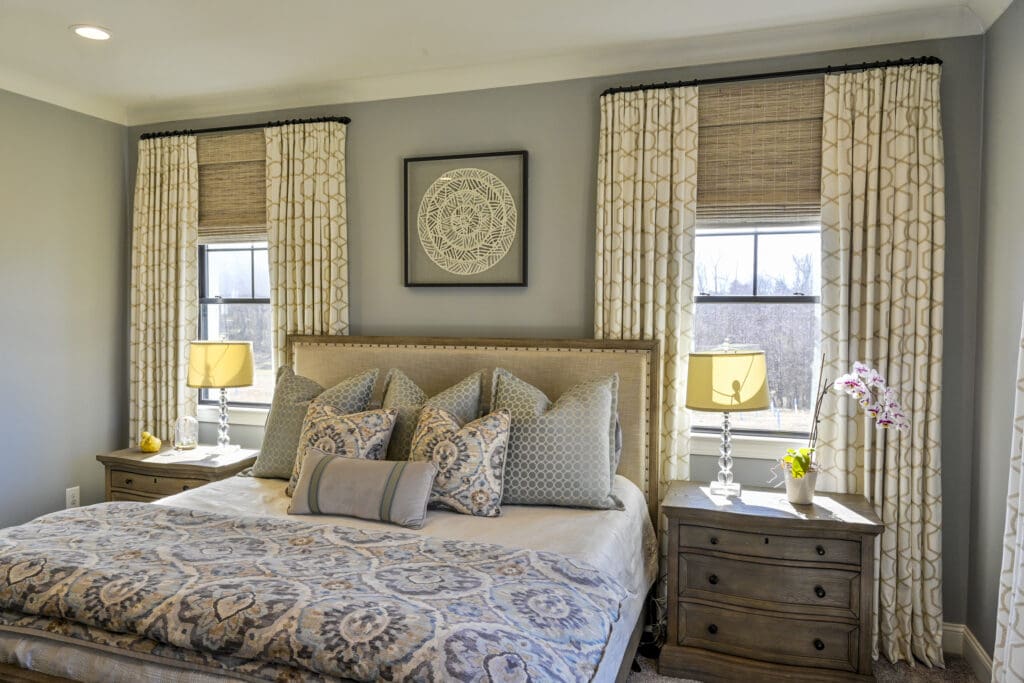 Layered window treatments with inside mount woven shades and custom drapery panels in a Greensboro bedroom