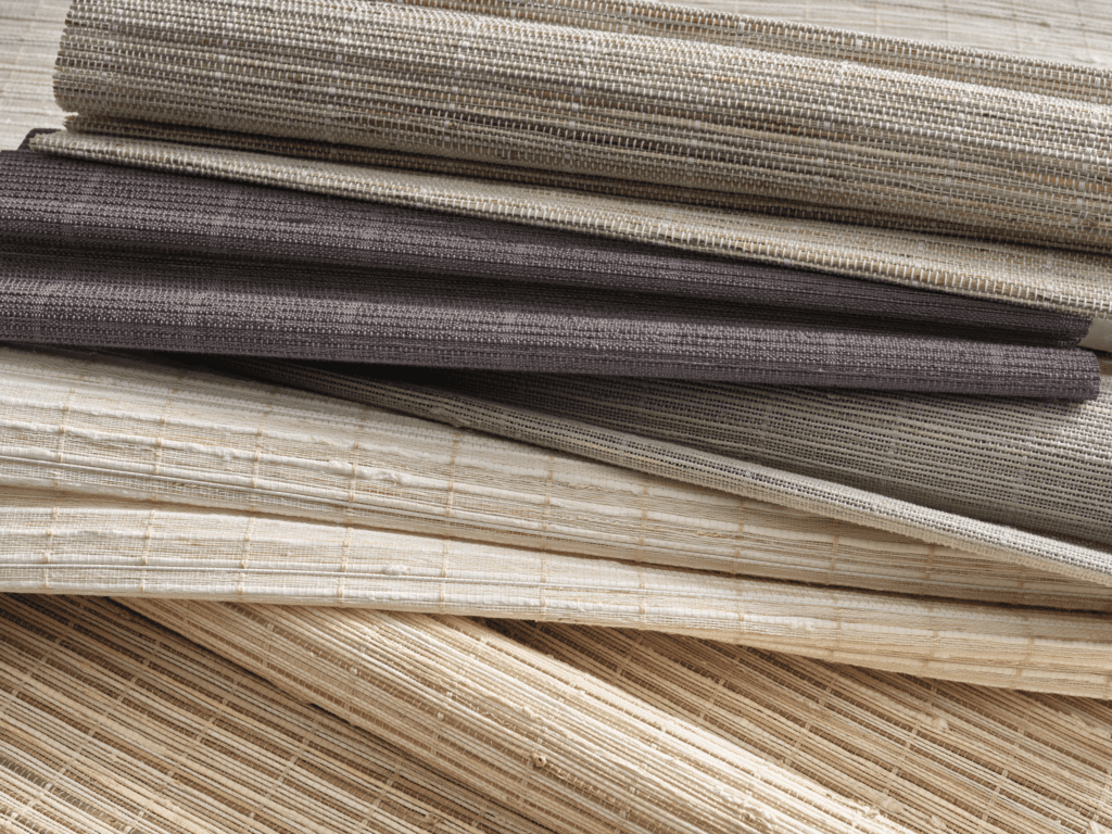 Rolled and stacked samples of woven textiles in neutral colors, including beige, gray, and brown shades, displayed on a flat surface.