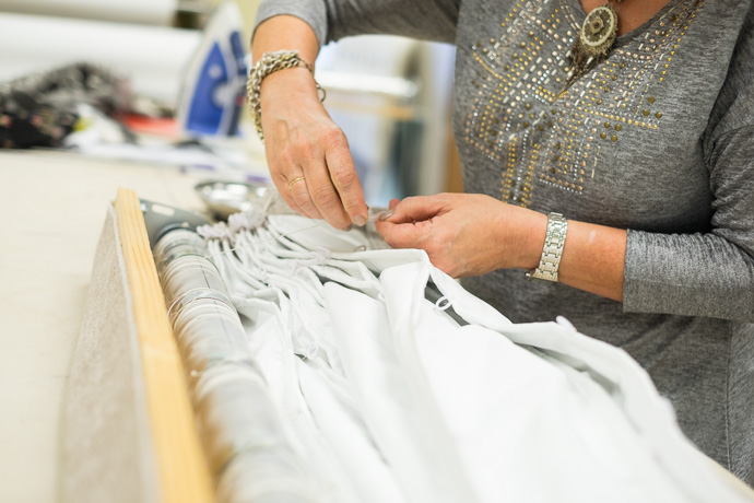 A person wearing a gray shirt and watch arranges white fabric and cords on a worktable, with an iron visible in the background.