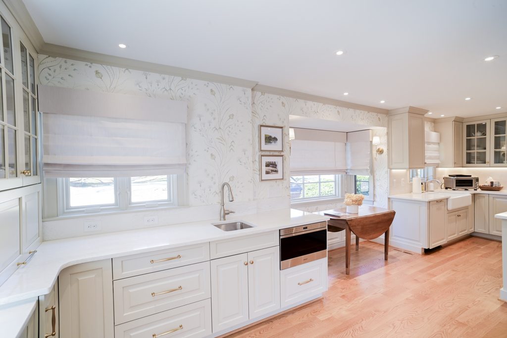 Bright, spacious kitchen with white cabinets, light wood flooring, under-cabinet sink, modern appliances, and large windows with white shades.
