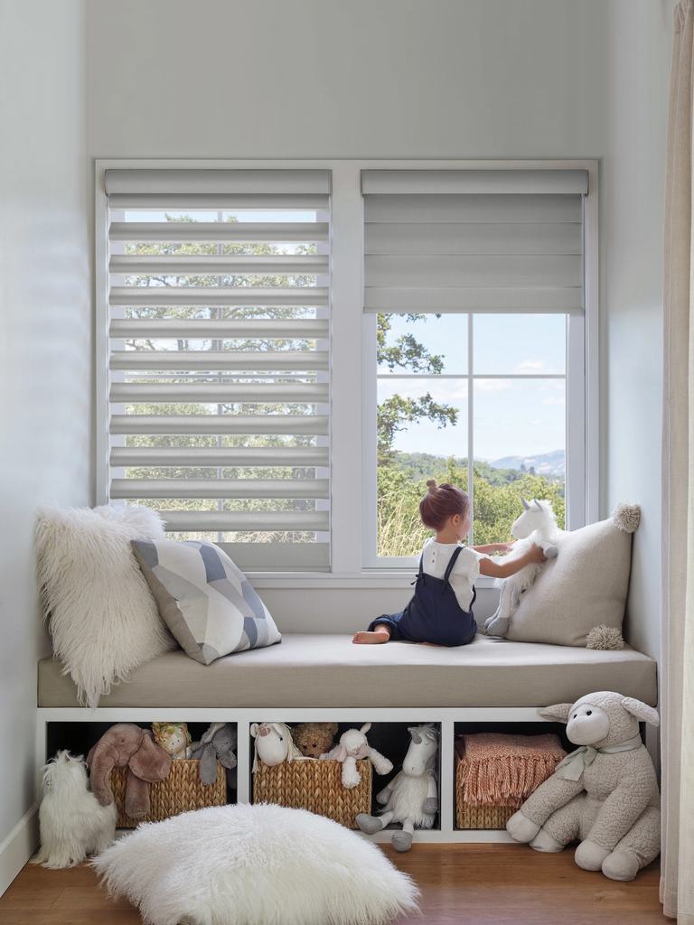 A child sits on a window seat playing with a unicorn plush toy, with storage baskets filled with stuffed animals underneath.