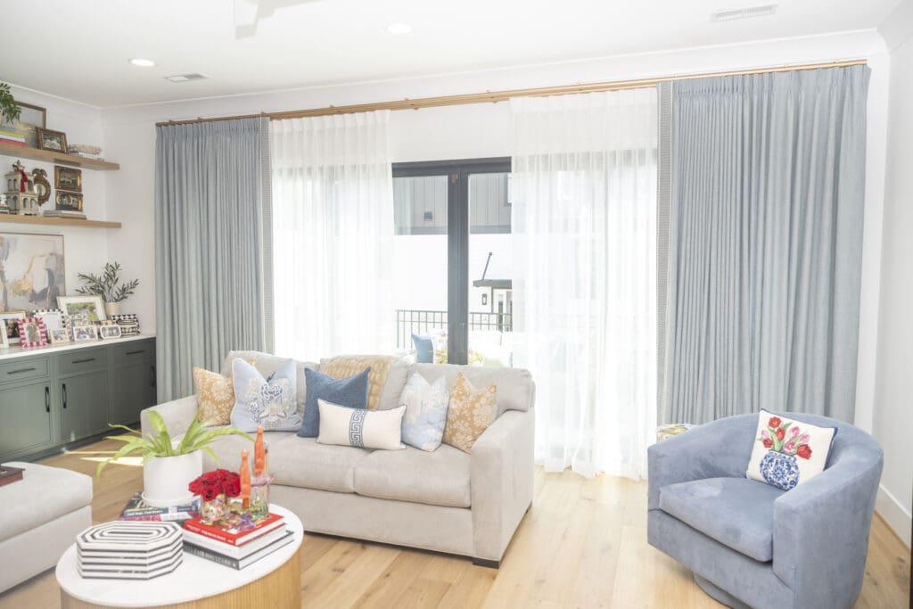 Living room with a light gray sofa and blue swivel chair facing a sliding glass door with light blue floor-to-ceiling curtains.